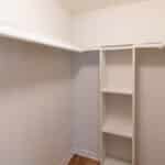 Empty walk-in closet with white walls and shelves, a built-in shelving unit with three open shelves in the corner, and light wood flooring.